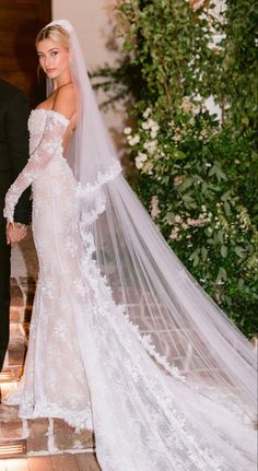 a bride and groom holding hands in front of an archway with greenery on either side