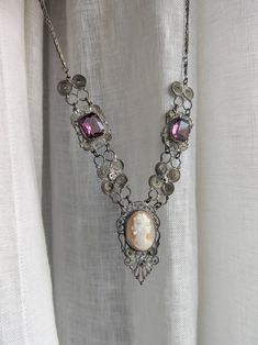 Antique necklace in silver tone metal filigree, mounted with a cameo and two purple glass stones. The stones have beautiful reflections and are in good condition. The necklace is not in excellent condition and shows signs of wear corresponding to its age, but it can still be worn and remains a very beautiful jewel. The metal is oxidized in several places and the chain has a damaged link, which however seems secure if not pulled (see last picture). Length: about 46 cm. Silver Metal Cameo Jewelry, Victorian Cameo Silver Necklace, Silver Cameo Metal Necklace, Silver Metal Cameo Necklace, Ornate Silver Amethyst Necklace, Formal Purple Metal Necklace, Vintage Purple Filigree Necklace, Purple Vintage Filigree Necklace, Cameo Necklace