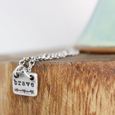 a silver charm with the words brave on it sitting on top of a piece of wood