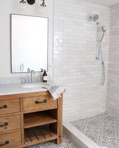 a bathroom with a sink, mirror and shower in it's corner area that has white tiles on the walls