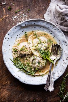 a white plate topped with ravioli covered in gravy and garnished with herbs