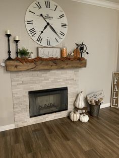 a clock on the wall above a fireplace with candles and pumpkins in front of it