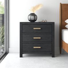 a black night stand with three drawers and a vase sitting on top of it next to a bed