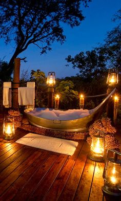 an outdoor bathtub with candles and towels on the deck outside at night, surrounded by trees