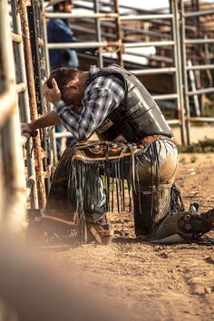 a cowboy leaning against a fence talking on his cell phone