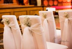 white chairs with bows and baby's breath flowers tied to them in a church