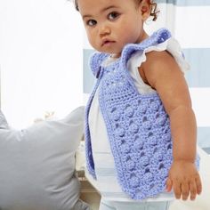 a small child wearing a blue crocheted vest and white shirt standing next to a pillow