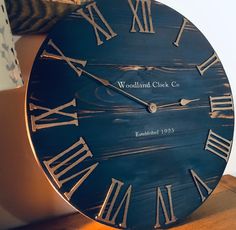 a blue clock with roman numerals on it sitting on a table next to a lamp