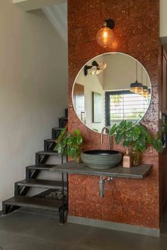 a round mirror hangs above a sink in a bathroom with stairs leading up to the second floor