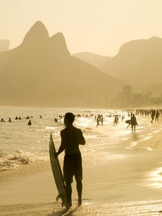 a man holding a surfboard while standing on top of a beach next to the ocean