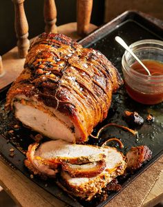 sliced pork with sauce and bread on a black platter next to a jar of ketchup