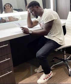 a man sitting at a desk in front of a mirror looking at his cell phone