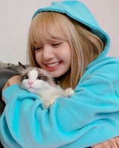 a woman holding a cat wrapped in a blue blanket and smiling at the camera while sitting on a couch