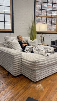 a woman laying on top of a large couch in a living room next to a window