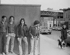 black and white photograph of four young men standing in front of a building with a dog