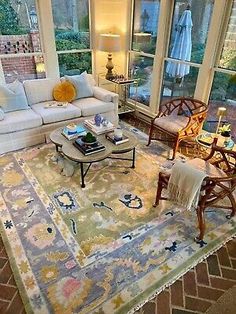 a living room filled with lots of furniture next to large windows and an area rug on the floor