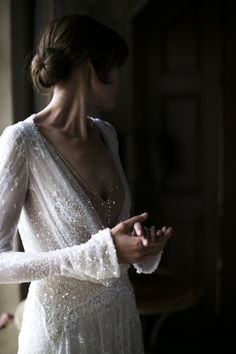 a woman in a white dress is looking down at her cell phone while wearing a long sleeved gown