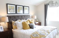 a bed with yellow and white pillows in a bedroom next to two framed pictures on the wall