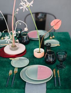 the table is set with plates, silverware and pink flowers in glass vases