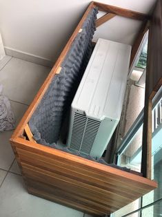 an air conditioner sitting inside of a wooden box on the floor next to a window