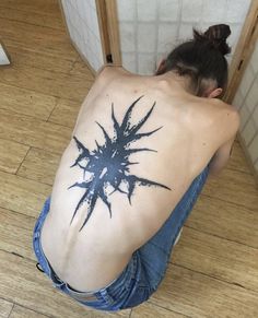 a woman with a tattoo on her back sitting on the floor in front of a mirror