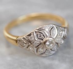 an antique diamond ring is sitting on a table with white and yellow gold trimmings