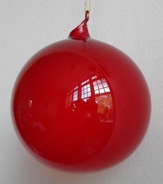 a red ornament hanging from a chain on a white wall in the shape of a ball