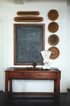 a chalkboard with writing on it in front of a wooden table and wall hangings