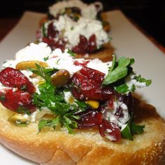 three pieces of bread with cranberry sauce and greens on top, sitting on a white plate