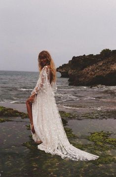 a woman in a white dress sitting on the rocks by the ocean with her legs crossed