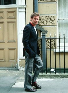 a man is standing on the sidewalk in front of a building wearing a suit and tie