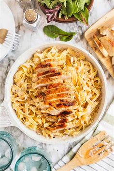 a bowl filled with chicken and noodles next to some salad on the side, along with utensils