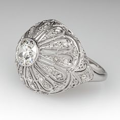 This marvelous circa 1920s ring features a domed gallery with a pierced design and bordered with milgrain edging. The ring is centered with one (1), bezel set, old European cut diamond. The center diamond is bordered with twenty-six (26), bead set, rose cut diamonds. The ring measures 18.4mm at the top, rises 8.4mm above the finger, tapering to 1.8mm wide and 1.1mm thick at the base of the shank. This ring is currently a size 8.5. Art Deco Halo Ring With Round Cut, Classic Domed Diamond Ring, Classic Dome Ring With Diamond Cut, Classic Oval Filigree Ring With Diamond Cut, Classic White Gold Dome Ring In Platinum, Classic White Gold Platinum Dome Ring, Classic Platinum Dome Ring, Elegant Domed Rings With Rose Cut Diamonds, Classic Dome Ring With Center Stone For Anniversary