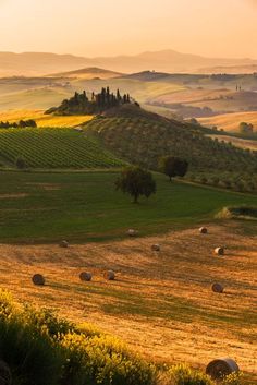 the rolling hills are dotted with bales of hay as the sun sets in the distance