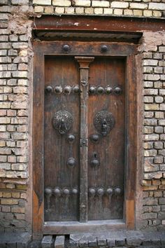 an old wooden door with metal knobs on the outside and brick wall behind it