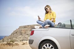 a woman sitting on the hood of a car looking at her cell phone