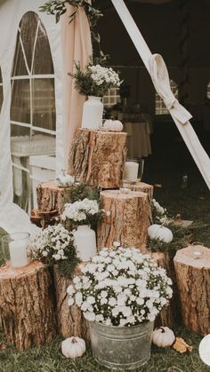 a wedding cake made out of logs and flowers in a bucket on the grass near a tent