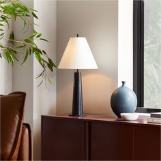 a table lamp sitting on top of a wooden cabinet next to a plant in a vase