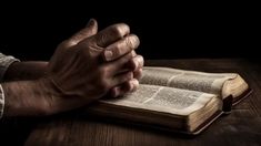 a person holding their hands over an open book on a table with dark background and light coming from the top