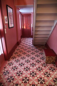 a hallway with red walls and black and white floor tiles on the ground next to stairs