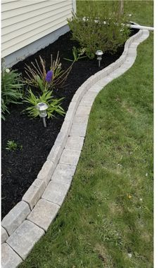 a small garden with flowers and plants in the grass next to a home's front yard