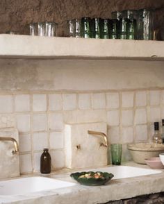 a kitchen counter with two sinks and bottles on the shelf above it, next to a bowl of food