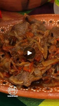 a brown bowl filled with meat and vegetables on top of a green tablecloth covered table