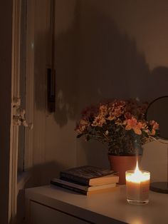 a lit candle sitting on top of a white table next to a vase with flowers