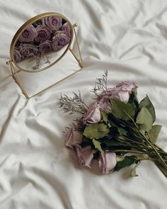 a bouquet of flowers sitting on top of a white sheet next to a mirror with purple roses in it