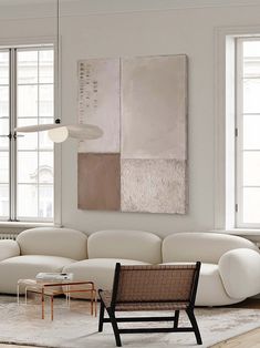 a living room filled with white furniture and large paintings on the wall above it's windows