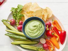 a plate filled with veggies and dip next to tortilla chips on a white table