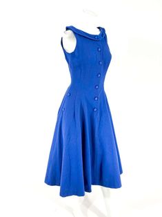 For Sale on 1stDibs - 1960s blue wool dress fitted to the waist with a flared skirt. The face of the dress has a button closure the goes down past the hip. The sides are adorned Blue A-line Vintage Fashion Dress, Blue A-line Dress With Buttons, Fitted A-line Blue Vintage Dress, Classic Blue Dress For Vintage Fashion, 1950s Style Buttoned Dresses For Work, A-line Vintage Dress With Buttons For Work, A-line Vintage Dress With Buttons, Classic Fitted Blue Vintage Dress, Vintage A-line Dress With Buttons For Workwear