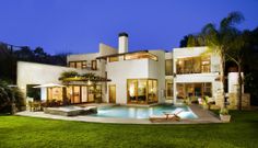 a large white house with a swimming pool in the front yard at night, surrounded by lush green grass and palm trees