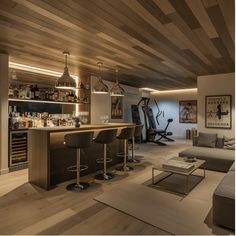 Home bar with stools, exercise equipment, and modern lighting in a cozy, wood-paneled basement.